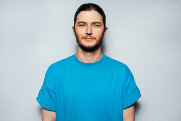 Fototapeta premium Portrait of young serious confident man in blue shirt on background of grey textured wall.