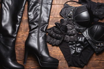 Various black leather clothes flat lay background. Bra, panties, high heels boots and stockings on...