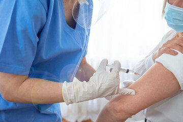 Professional doctor or nurse giving flu or COVID-19 injection to patient. Woman in medical face mask getting antiviral vaccine at hospital or health center during vaccination and immunization campaign