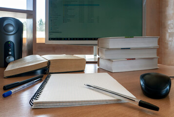 Working environment. A monitor, books, notebook, pen and other items are on a wooden table. The...