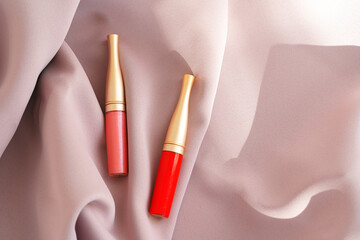 Naklejka premium Lip gloss make up products on pink silky cloth