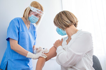 Professional doctor or nurse giving flu or COVID-19 injection to patient. Woman in medical face mask getting antiviral vaccine at hospital or health center during vaccination and immunization campaign