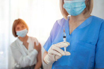 Closeup of a nervous woman and her doctor wearing face masks and getting a vaccine shot in a...