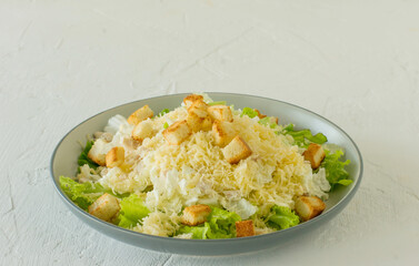 Traditional caesar salad in a plate on a white table with leaves, sauce, croutons and parmesan.