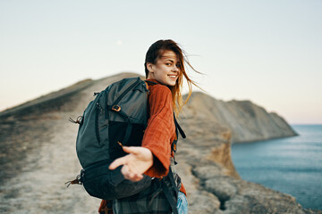 woman climbs the mountains near the sea with a backpack on her back looking back