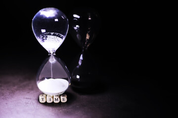 Sand running through the bulbs of an hourglass measuring the passing time in a countdown to a deadline, on a dark table background with copy space.