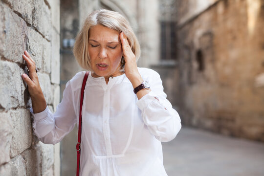 Elderly woman with headache on a city street. High quality photo