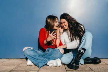 Couple of friends with long hair, one blonde and the other brunette, listening to music from their cell phones.