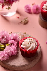 Fototapeta na wymiar Red velvet cupcake on a gray plate, near sakura flowers, on a pink background.