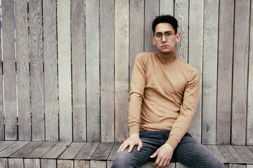 Young handsome guy posing at the camera. Male student pondering business problem solution schemes. Gay on a wooden background.