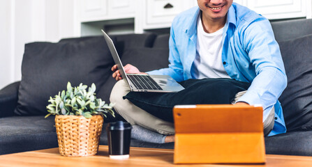Handsome asian businessman looking at technology of tablet computer monitor while sitting on sofa.Young creative coworkers business people working and typing on keyboard at home
