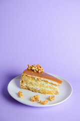 One piece of Caramel cake with pop corn on top served on a white plate. Over pastel violet purple background.