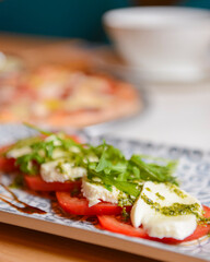 Classic caprese salad on table with pizza. Photo with blurred background. Traditional Italian cuisine concept.