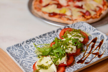 Classic caprese salad on table with pizza. Photo with blurred background. Traditional Italian cuisine concept.