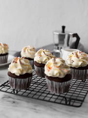 Chocolate cupcakes on a black metal grill on a light background with a coffee pot