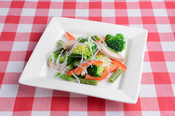 Mixed Salad on White Plate with mixed greens, cucumber, brocolli, squash and carrots served on red plaid table cloth.