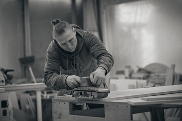 Close up. Carpenter at workshop polishes wooden board with a electric orbital sander. Woodwork and furniture making concept. black and white photography