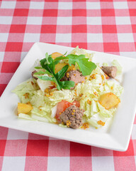 Fresh salad with beef served in a white plate plate on red plaid table cloth. Italian cuisine concept.