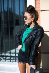 female in black leather jacket, shorts and fashionable sunglasses staying on the stairs near closed shop