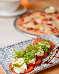 Classic caprese salad on table with pizza. Photo with blurred background. Traditional Italian cuisine concept.