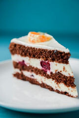 A piece of chocolate cake with vanilla cream. Berries inside and a piece of tangerine on top.