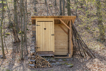 Rustic wooden toilet in the forest with a heart-shaped hole in the door boards. Wooden outhouse in the nature.