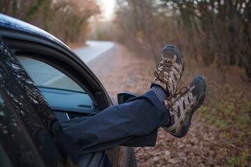 male feet in trekking boots sticking out the car window.