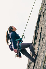 Female climber looks up tiredly hanging from climbing rope in safety.