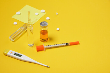 pills, electronic thermometer, ampoules with medicine and a syringe on a yellow background copy space top view