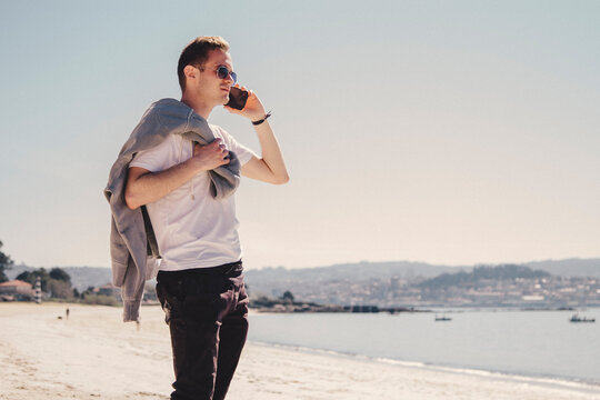 Young Man Walking On The Beach Talking On The Mobile Phone