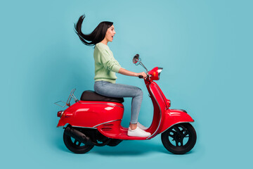 Fototapeta na wymiar Profile side view of attractive cheerful amazed girl riding moped fast speed air blowing hair isolated over bright blue color background