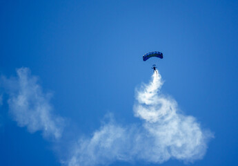 Parachute Regiment Freefall Team member of 'The Red Devils' practises with smoke trails over Netheravon Airfield, Salisbury Plain military training grounds under a cloudless bright blue sky 