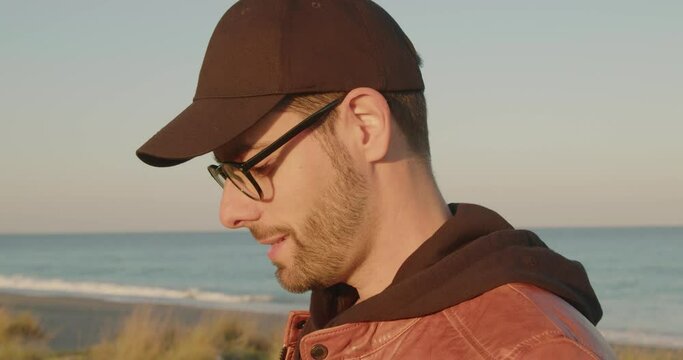 Giovane ragazzo con occhiali e cappello pilota il drone in spiaggia vicino al mare