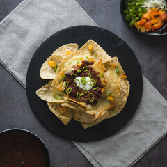 Overview of a plate of nachos with vegetables, cheese and beans