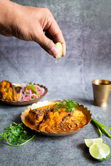 chef preparing Indian fish curry and squeezing lemon on top