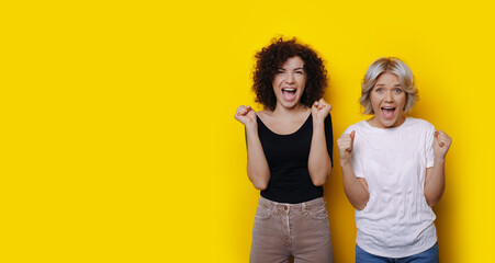 Obraz na płótnie Canvas Curly haired friends are shocked by something posing on a yellow studio wall