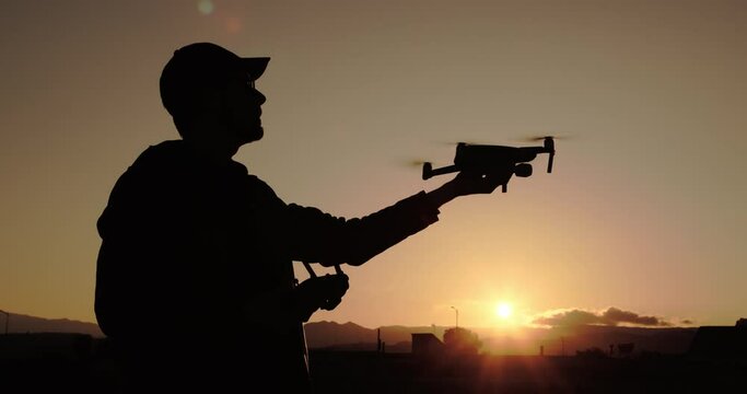Sagoma di un ragazzo mentre pilota il drone al tramonto