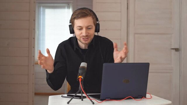 Young hipster man with headphones recording podcast using laptop at home studio, broadcasting an interview using microphone