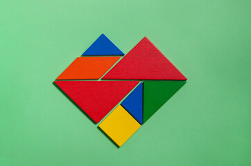 Heart of colorful tangrams in green background 