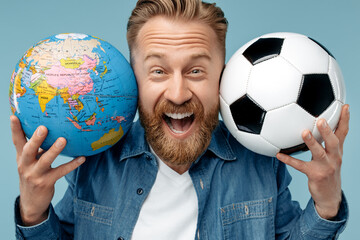 Close-up portrait of bearded blonde hipster man holding classic soccer ball and world globe over blue background.