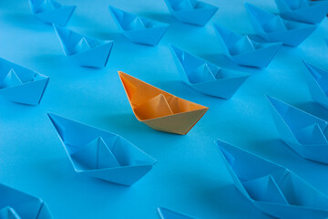 Origami in blue and orange on a blue paper background. An orange paper boat among many blue ones. Teamwork concept. Concept to stand out from the crowd.