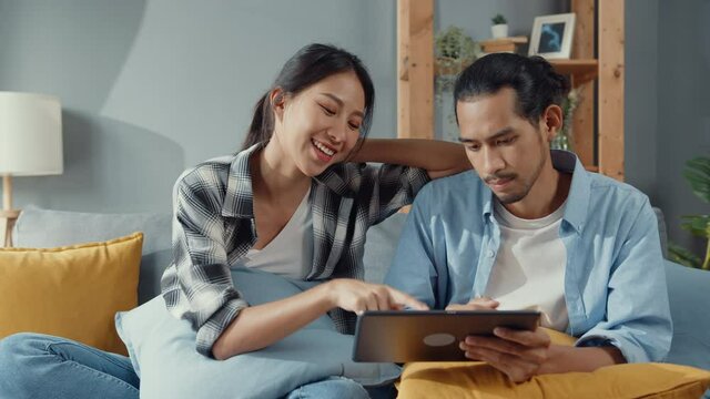 Happy asia young attractive couple man and woman sit on couch use tablet shopping online furniture decorate home in the living room at new house. Young married moving home shopper online concept.
