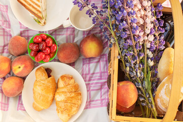 Romantic picnic for a couple. Basket with flowers, wine, peaches, sandwiches on the tablecloth on a Sunny day, top view