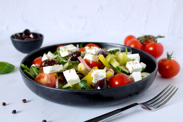 Mediterranean greek salad with fresh vegetables, feta cheese and olives on a white plate. Green vegetable salad, feta cheese and olive oil on a white plate, copy space