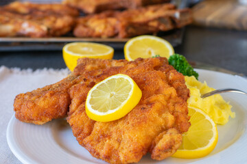 fried and breaded cutlet with mashed potatoes and lemon served on plate with table background