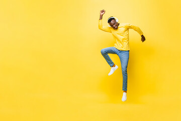 Happy energetic young African man wearing headphones listening to music and jumping with hand up...