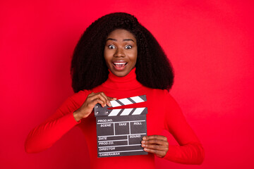Portrait of astonished dark skin person open mouth hands hold clapboard isolated on red color...