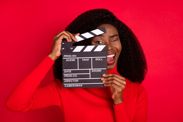 Photo of carefree crazy dark skin person hold clapboard near eye open mouth isolated on red color...