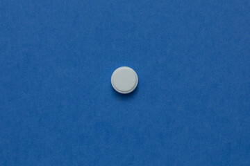white round pill on a blue background. A small round mass of solid medicine.