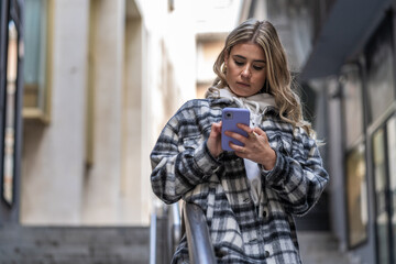 Pretty Caucasian young woman with coat and smartphone in hand